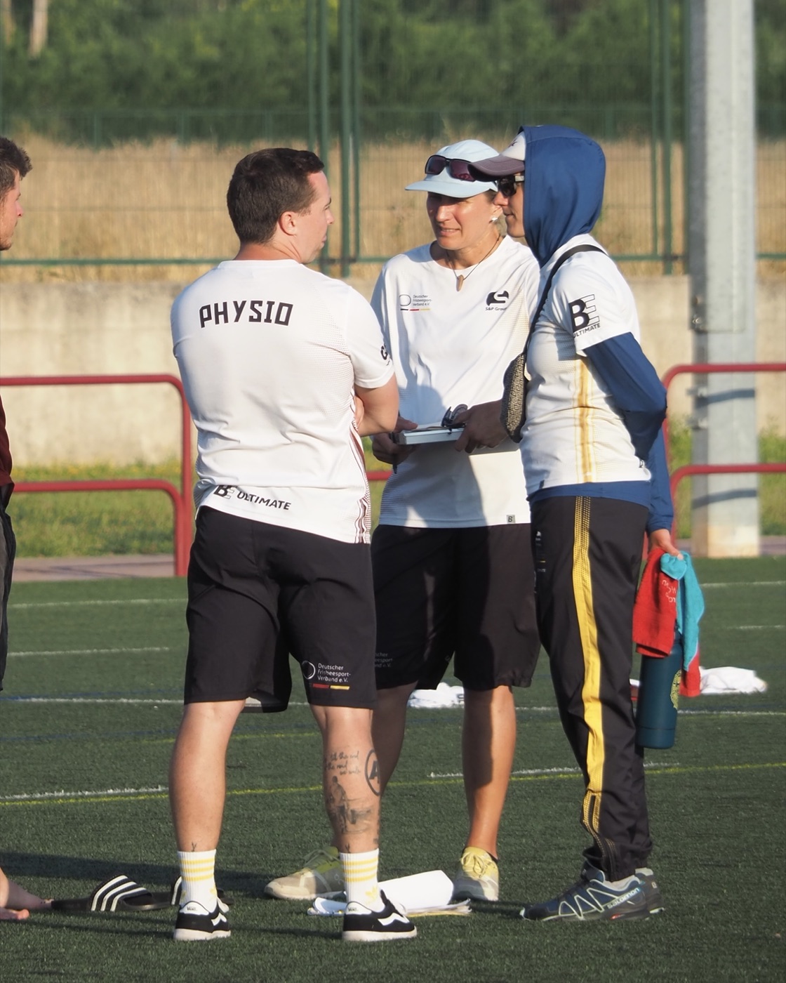 Ronnie Nolte im Physio-Shirt des Deutschen Frisbeesport-Verbands im Gespräch mit den beiden Nationalcoaches am Spielfeldrand